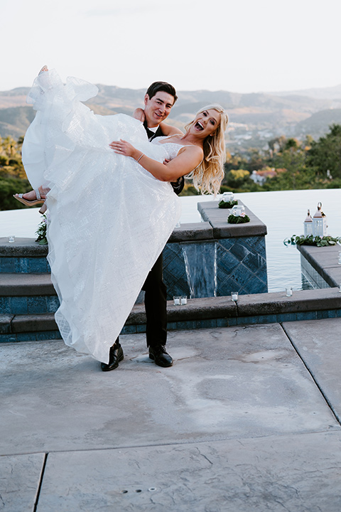 bride in a white ballgown with a strapless neckline and a long veil and the groom in a notch lapel tuxedo and black bow tie dancing 