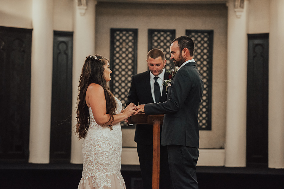  bride in a formfitting white lace gown with a long train and the groom in a dark blue suit 