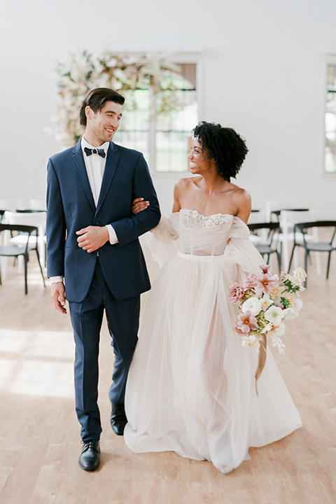  bride in a tulle ballgown with an off the shoulder detail and full billowed sleeves walking away from the altar together