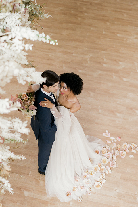  bride in a tulle ballgown with an off the shoulder detail and full billowed sleeves and the groom in a slate blue suit with a matching bow tie dancing