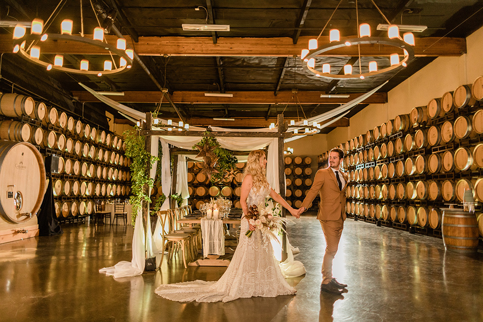 bride in a lace bohemian gown and the groom in a caramel brown suit with a chocolate brown long tie and fun pocket square in the winery