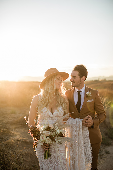   bride in a lace bohemian gown and the groom in a camel colored suit with a dark brown long tie and fun pocket square outside