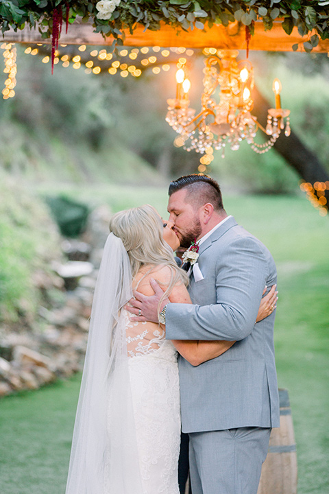  bride in a white lace mermaid style gown and a strapless neckline and groom in a light grey suit at the ceremony