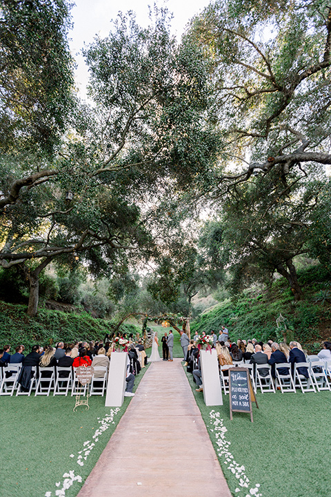  bride in a white lace mermaid style gown and a strapless neckline and the groom in a light grey suit at the ceremony