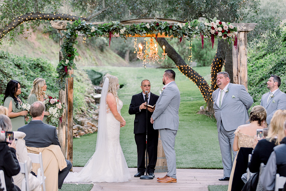  bride in a mermaid style lace white gown and the groom in a light grey suit with a light brown shoes and white pocket square, the bridesmaids in sage green dresses and the groomsmen in light grey suits and bow ties