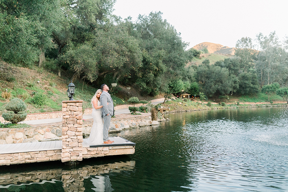  bride in a mermaid style lace white gown and the groom in a light grey suit with a light brown shoes and white pocket square, the bridesmaids in sage green dresses and the groomsmen in light grey suits and bow ties