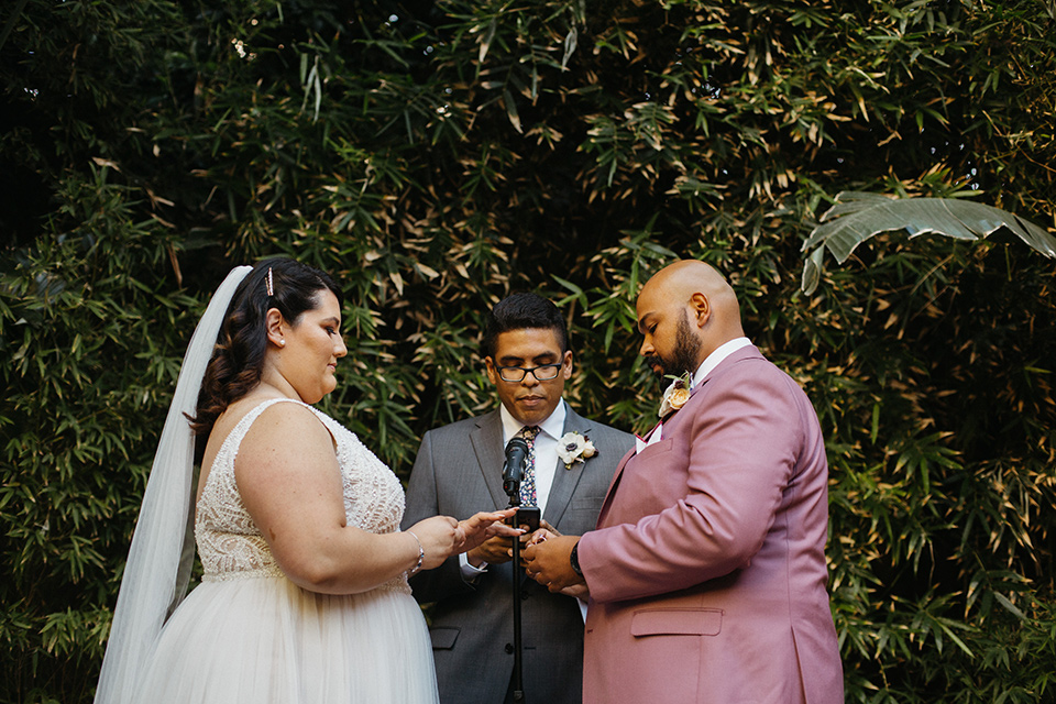  bride in a tulle ballgown with cap sleeves and the groom in a rose pink suit at the ceremony