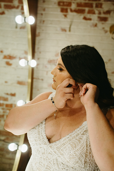  bride in a tulle ballgown with cap sleeves putting on her earrings