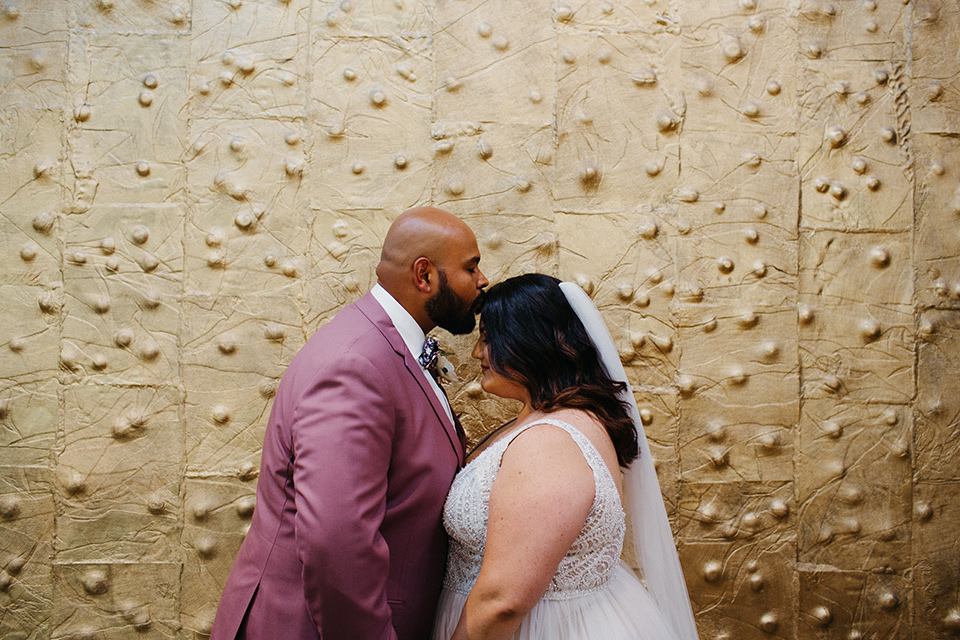  bride in a tulle ballgown with cap sleeves and the groom in a rose pink suit at the ceremony