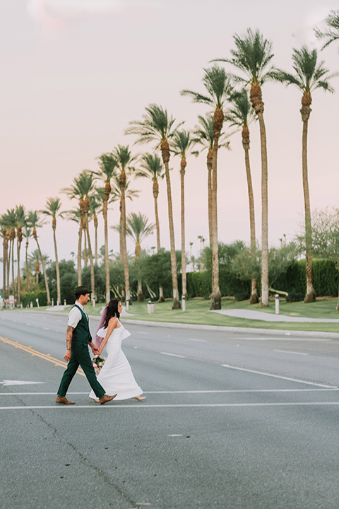  bride in a white bohemian gown with one sleeve and a ruffled detail the groom in a green suit with a white shirt and bolo tie