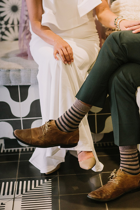  bride in a white bohemian gown with one sleeve and a ruffled detail the groom in a green suit with a white shirt and bolo tie