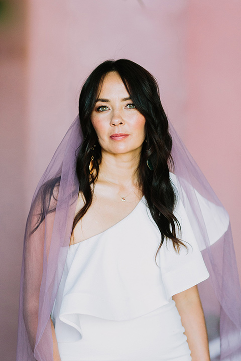  bride in a white bohemian gown with one sleeve and a ruffled detail with a pink veil