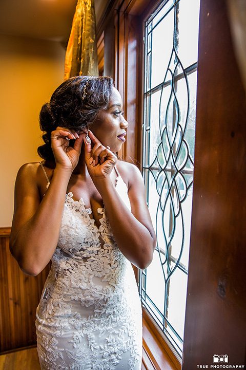  bride in a white formfitting gown with a plunging neckline and lace detailing and the groom in a white lace tuxedo with a black shirt and gold bow tie, kissing on the steps