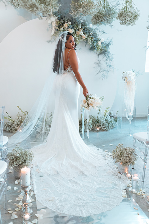  bride in a formfitting satin gown and a cathedral length veil and the groom in a light grey peak lapel suit with a teal blue bow tie 