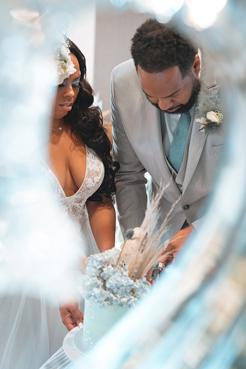  bride in a formfitting satin gown and a cathedral length veil and the groom in a light grey peak lapel suit with a teal blue bow tie 