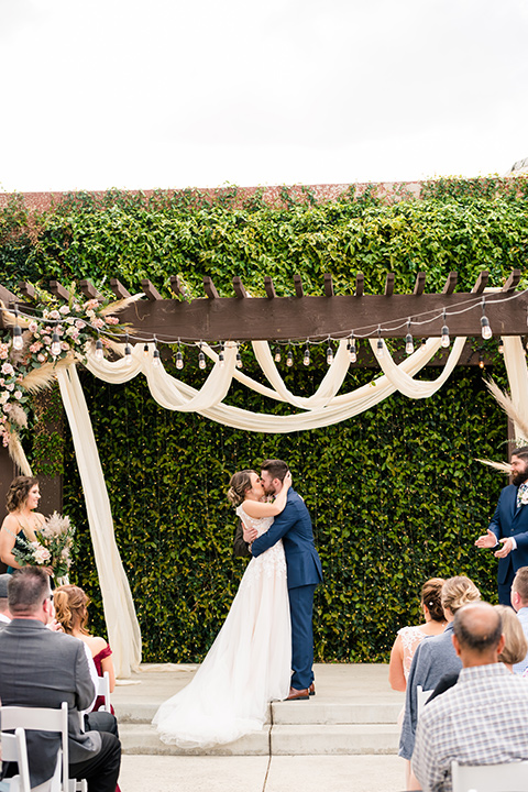  groom in a dark blue suit with a blue bow tie and the bride in a lace gown with a high neckline 