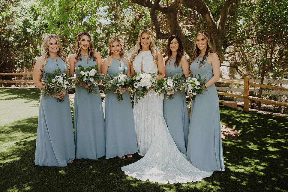  =” the bride in a flowing white gown with a high lace neckline and a long cathedral veil, the bridesmaids in dusty blue long gowns