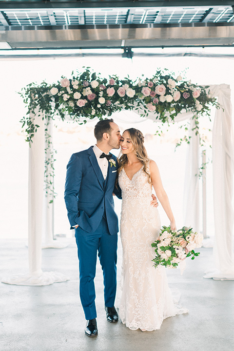  bride in an ivory lace gown with a modern geometric pattern and a v neckline, the groom wore a cobalt blue suit with a black bowtie kissing