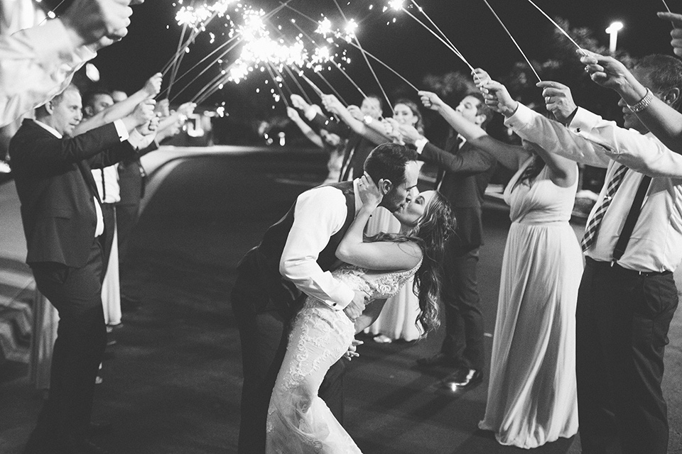  bride in an ivory lace gown with a modern geometric pattern and a v neckline, the groom wore a cobalt blue suit with a black bowtie kissing with sparklers 