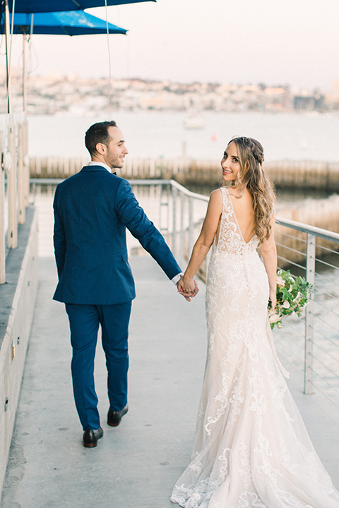  bride in an ivory lace gown with a modern geometric pattern and a v neckline, the groom wore a cobalt blue suit with a black bowtie walking