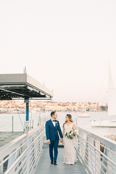  bride in an ivory lace gown with a modern geometric pattern and a v neckline, the groom wore a cobalt blue suit with a black bowtie walking towards camera