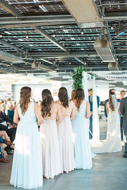  bride in an ivory lace gown with a modern geometric pattern and a v neckline and bridesmaids in pastel dresses 