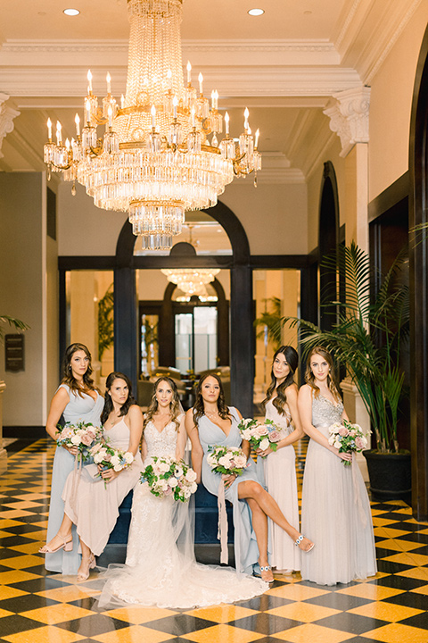  bride in an ivory lace gown with a modern geometric pattern and a v neckline and the bridesmaids in pastel gowns