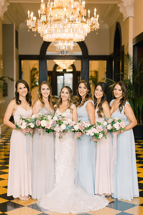  bride in an ivory lace gown with a modern geometric pattern and a v neckline and bridesmaids in pastel dresses 