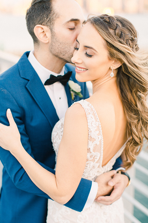  bride in an ivory lace gown with a modern geometric pattern and a v neckline, the groom wore a cobalt blue suit with a black bowtie walking by ceremony space