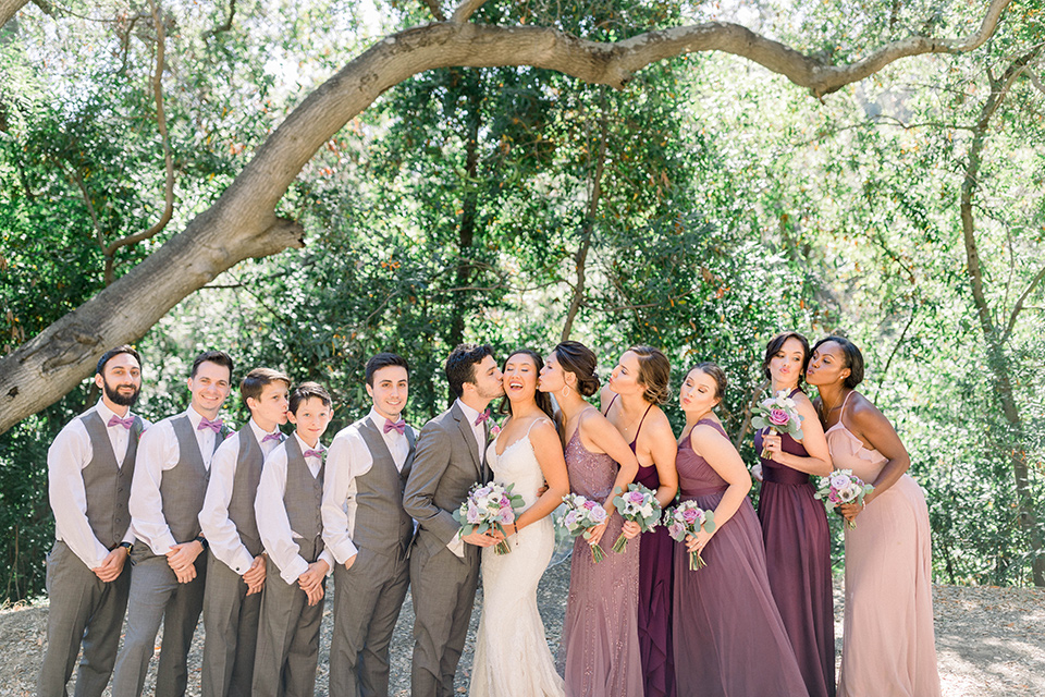  bride in a white lace formfitting gown with thin straps, the groom in a café brown suit with a purple bow tie, the bridesmaids wore mauve and pink dresses and groomsmen wore a laid back look with café brown pants and vest with purple bow ties