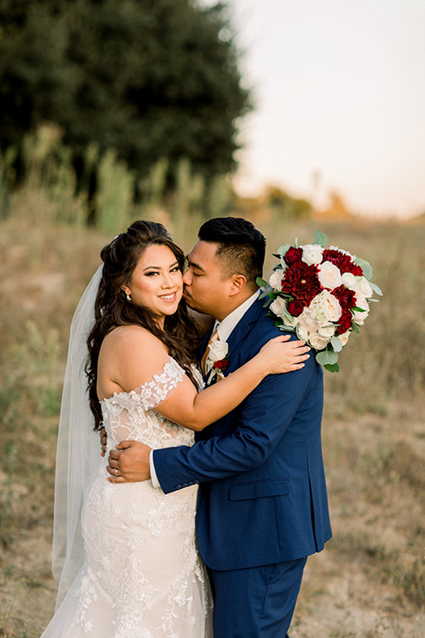  bride in a Spanish style lace gown and the groom in a cobalt suit with a pink tie, they embrace 