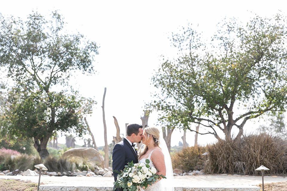  bride in a white lace gown and the groom in a navy shawl lapel tuxedo and blow tie kissing