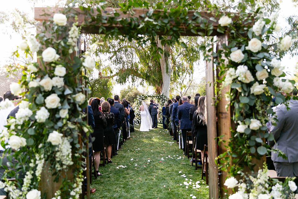  bride in a white lace gown and the groom in a navy shawl lapel tuxedo and blow tie, bridesmaids in navy gowns and groomsmen in black tuxedos