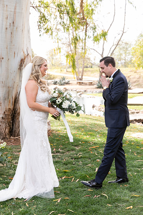  bride in a lace gown and long veil, groom in a navy shawl lapel tuxedo with a black bow tie – first look 