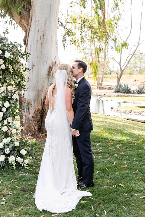  bride in a white long lace gown with a long veil and the groom in a navy shawl lapel tuxedo