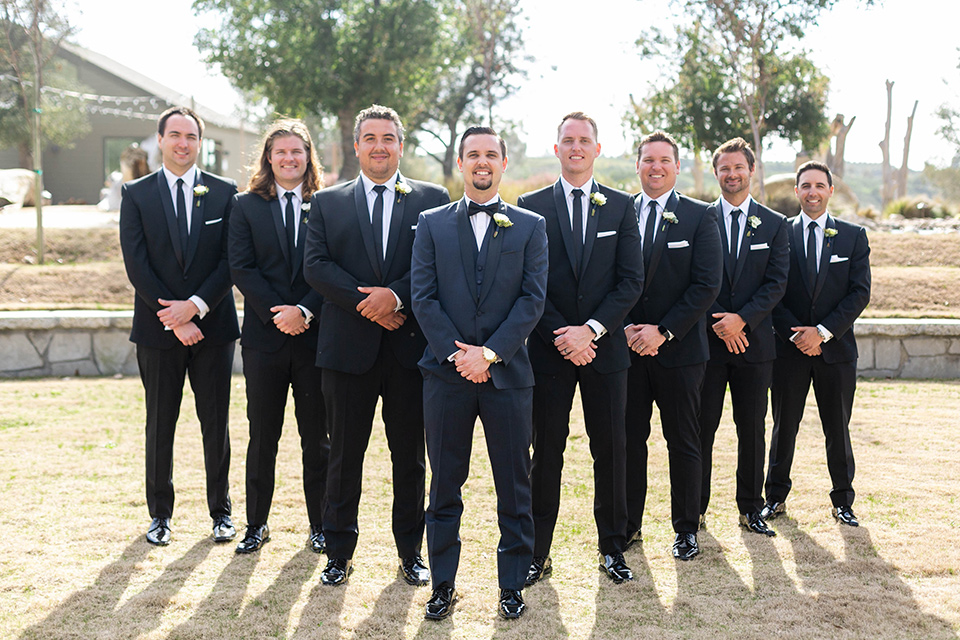  groom in a navy shawl lapel tuxedo and groomsmen in black tuxedos