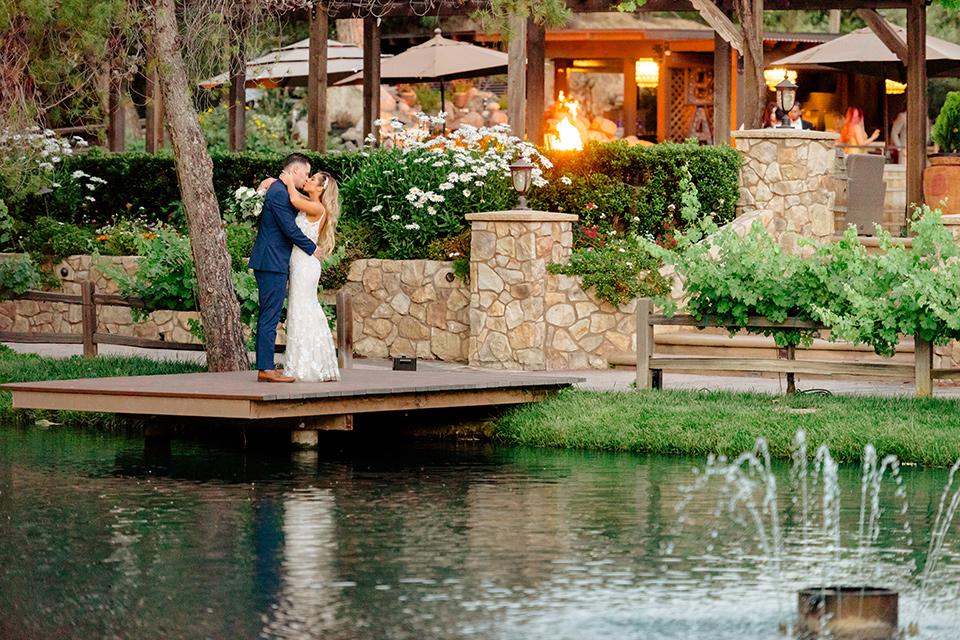  bride in a white lace gown with a long train and veil, groom in a cobalt blue suit with a blue floral long tie on the water 