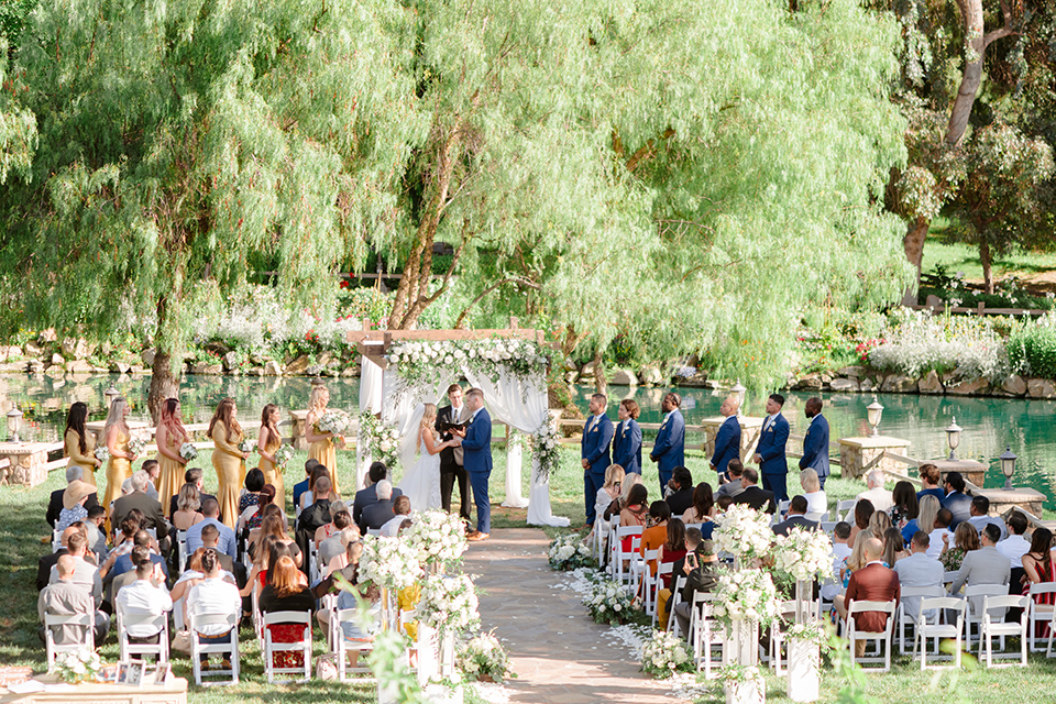  bride in a white lace gown with a long train and veil, groom in a cobalt blue suit with a blue floral long tie at the ceremony 