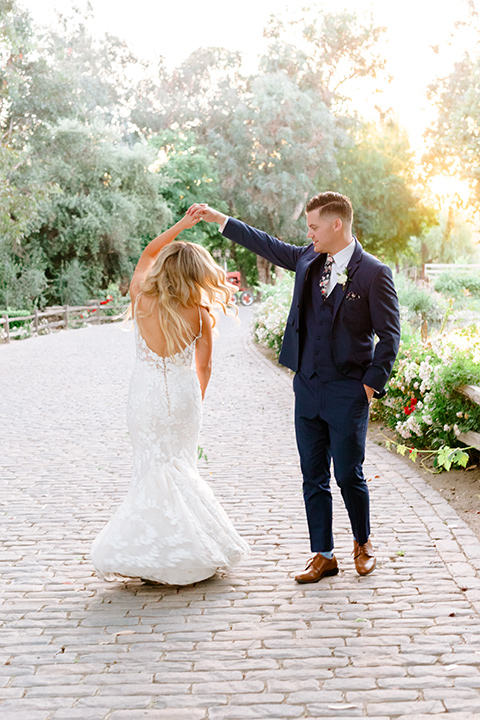  bride in a white lace gown with a long train and veil, groom in a cobalt blue suit with a blue floral long tie dancing