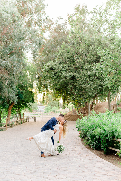  bride in a white lace gown with a long train and veil, groom in a cobalt blue suit with a blue floral long tie dancing 