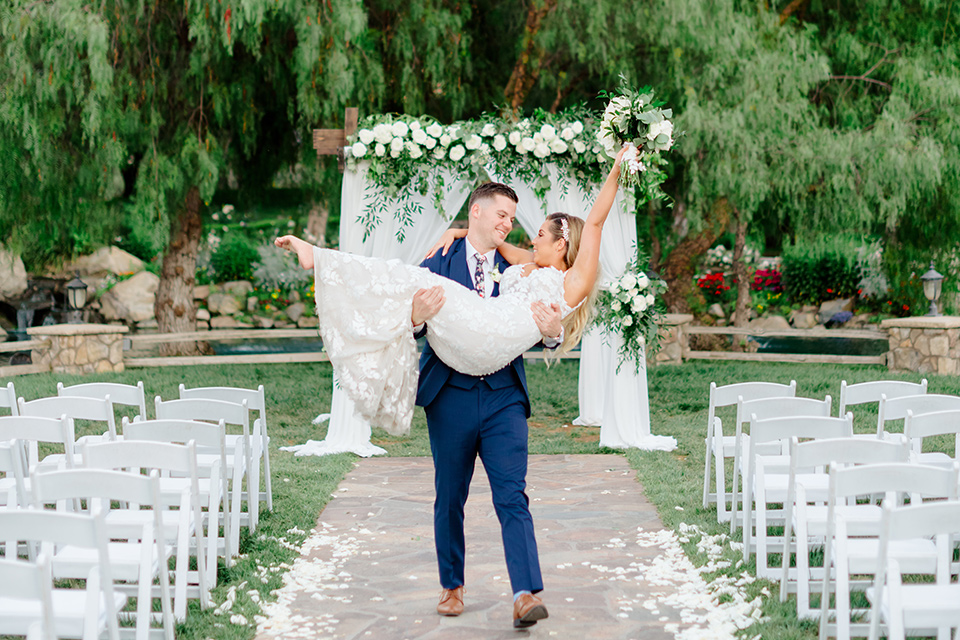  bride in a white lace gown with a long train and veil, groom in a cobalt blue suit with a blue floral long tie, the bridesmaids in a gold ballgowns and groomsmen in cobalt blue suit with blue floral bow ties 