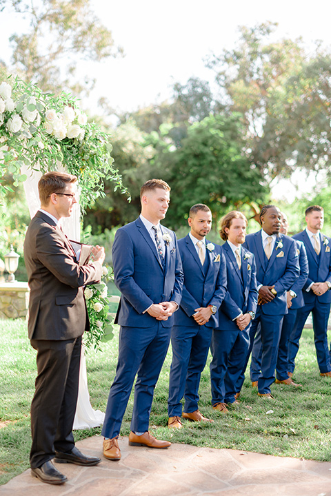  groom in a cobalt blue suit with a blue floral long tie and groomsmen in blue suits with floral bow ties