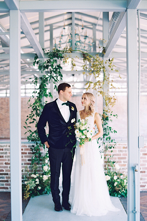  bride in a formfitting gown with long cathedral veil and the groom in a black velvet tuxedo