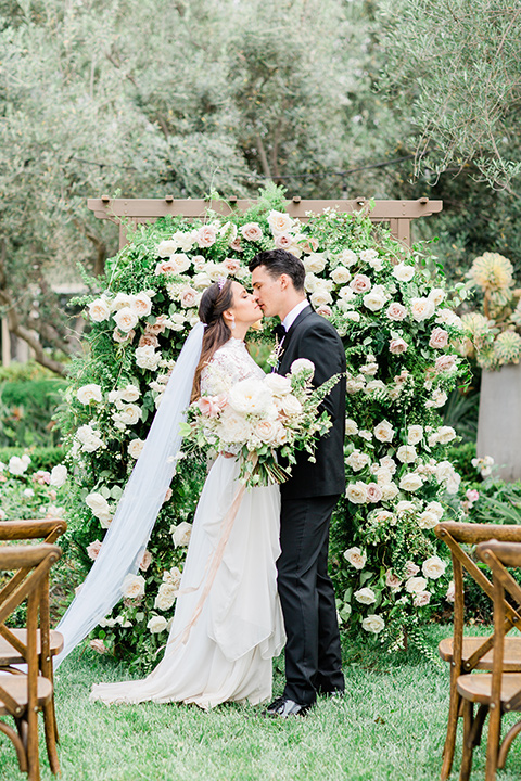  bride in a European inspired gown with lace details, a high neckline, and long sleeves and the groom in a black tuxedo and a black bow tie 