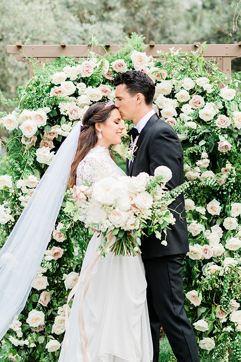  bride in a European inspired gown with lace details, a high neckline, and long sleeves and the groom in a black tuxedo with a black bow tie 