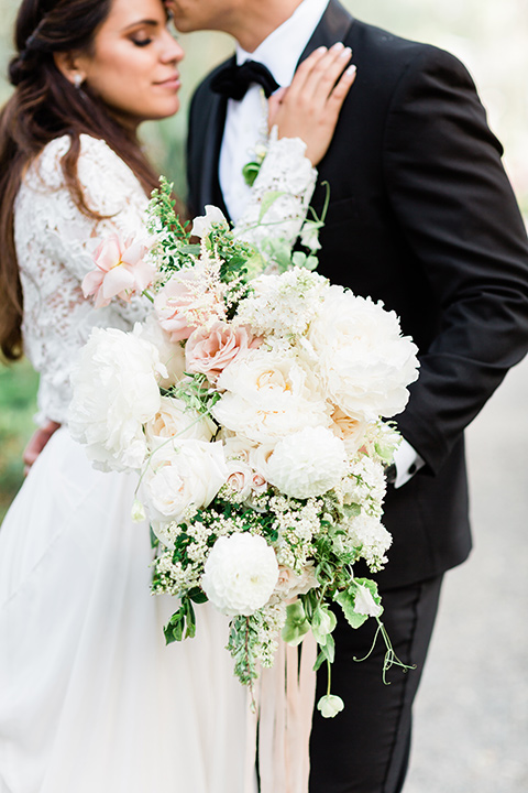  bride in a European inspired gown with lace details, a high neckline, and long sleeves and the groom in a black tuxedo with a black bow tie 