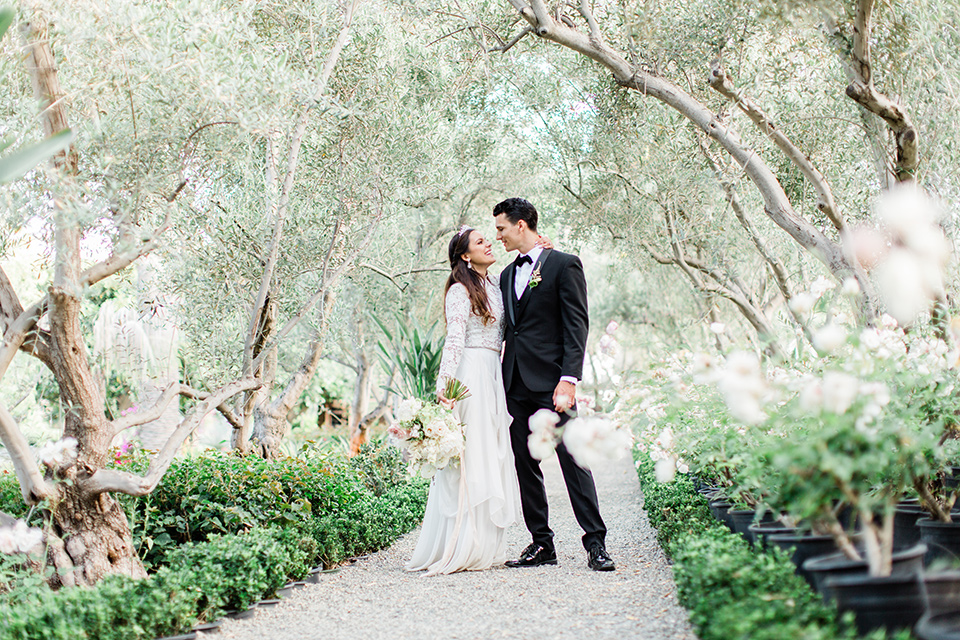  bride in a European inspired gown with lace details, a high neckline, and long sleeves and the groom in a black tuxedo and a black bow tie 