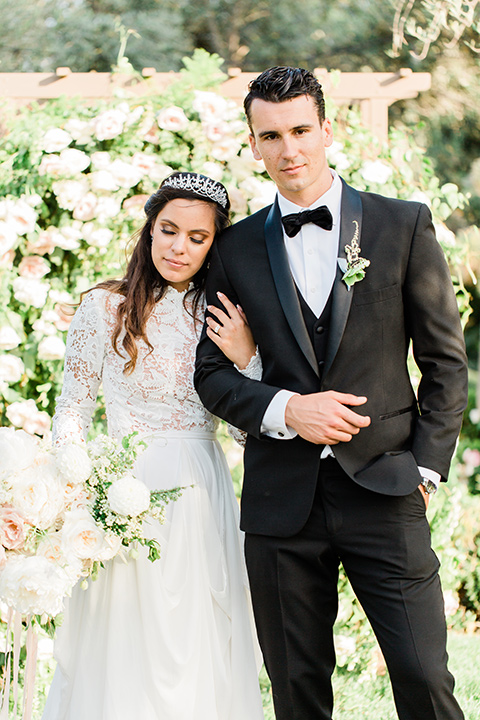  bride in a European inspired gown with lace details, a high neckline, and long sleeves and the groom in a black tuxedo and a black bow tie 