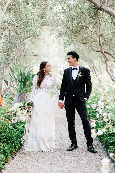  bride in a European inspired gown with lace details, a high neckline, and long sleeves and the groom in a black tuxedo with a black bow tie 