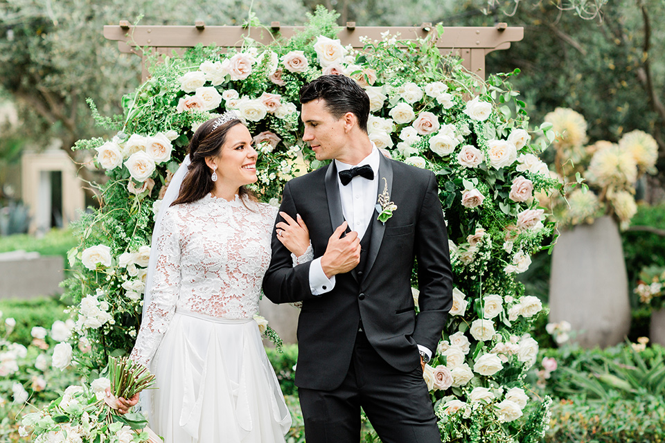  bride in a European inspired gown with lace details, a high neckline, and long sleeves and the groom in a black tuxedo and a black bow tie 